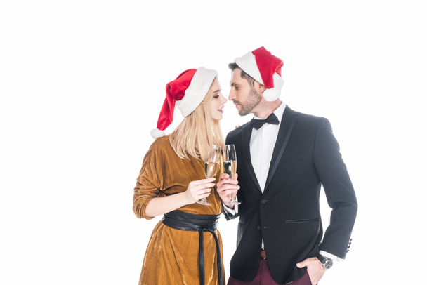 portrait of stylish couple in santa claus hats clinking glasses of champagne isolated on white - Foto, Imagem