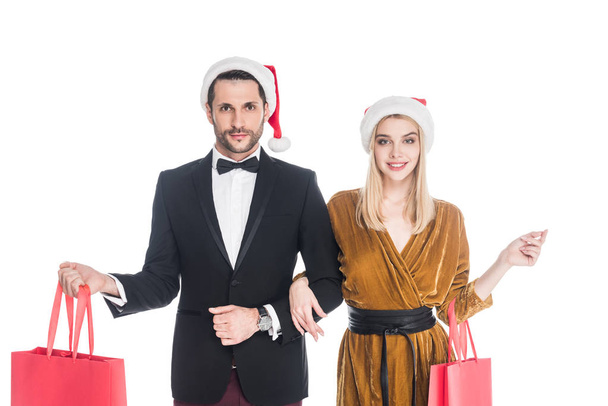 portrait of attractive couple in santa claus hats with shopping bags isolated on white - Foto, afbeelding