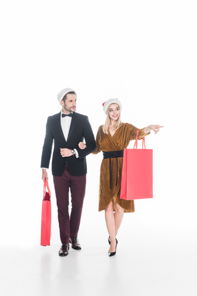attractive couple in santa claus hats with shopping bags isolated on white - Photo, Image