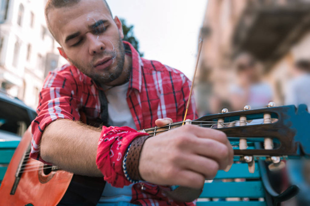 Focused street musician preparing guitar before performance - Фото, зображення