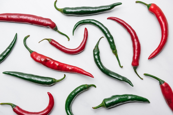 top view of red and green chili peppers on white marble surface - 写真・画像