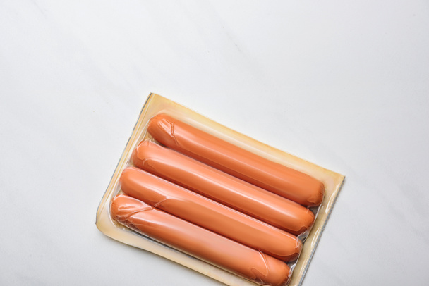 top view of plastic package of sausages on white marble surface - Фото, зображення