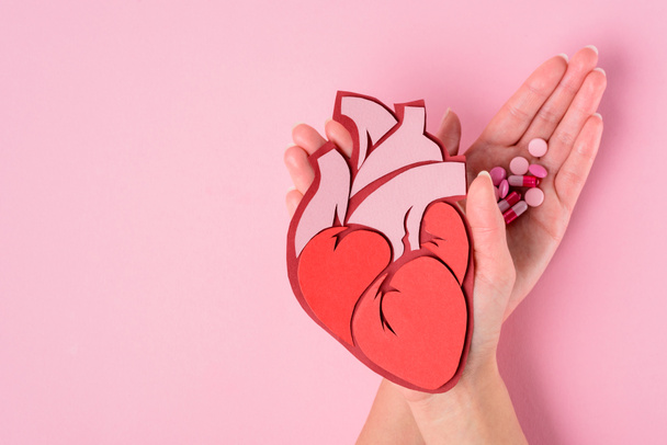 bijgesneden afbeelding van vrouw met anatomisch menselijk hart en verschillende pillen op roze  - Foto, afbeelding