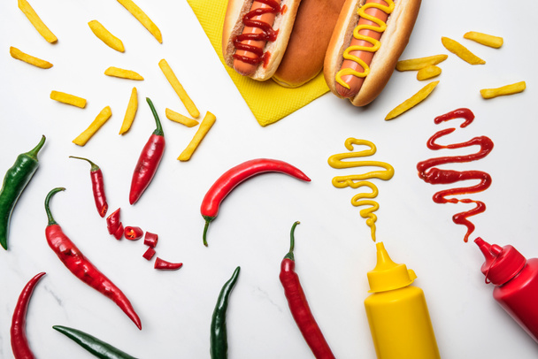 Blick von oben auf köstliche Hot Dogs und Paprika mit Senf und Ketchup auf weißem Marmor - Foto, Bild