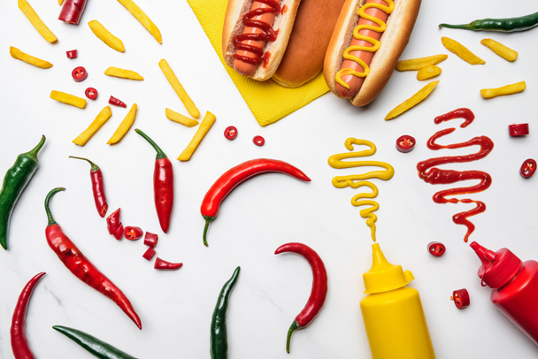 vista superior de deliciosos hot dogs, pimientos y papas fritas con mostaza y ketchup en la superficie blanca
 - Foto, imagen