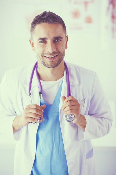 Young and confident male doctor portrait standing in medical office. - Φωτογραφία, εικόνα