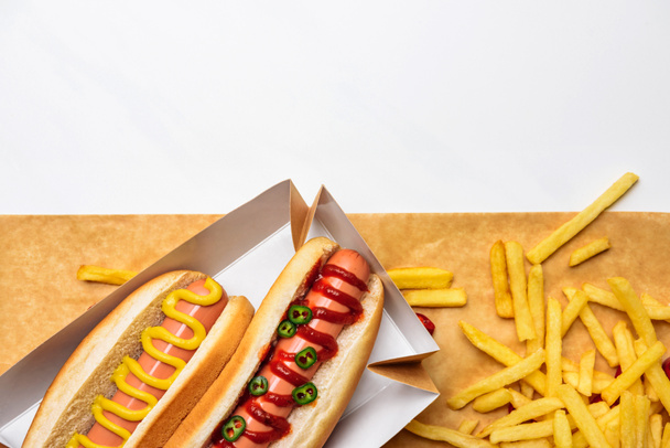 top view of spicy hot dogs with french fries on parchment paper isolated on white - Fotó, kép