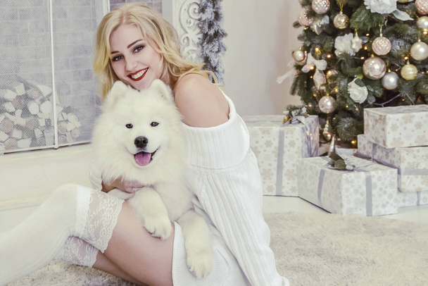 krásná blondýnka v bílých šatech s bílou husky na pozadí krb a vánoční tre - Fotografie, Obrázek