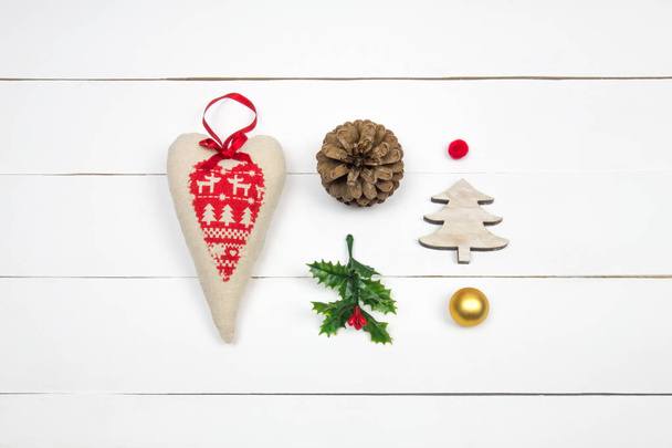 Creative Christmas layout. Red patchwork heart, mistletoe, pinecone, christmas tree and balls on white wood background. Flat lay top view.  - Photo, Image
