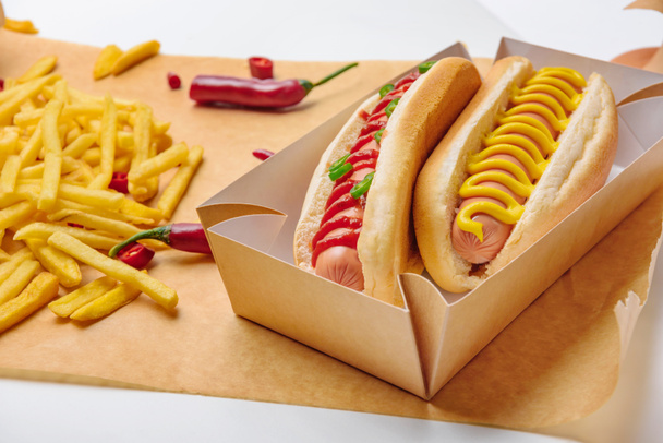 close-up shot of spicy hot dogs with french fries on parchment paper - Photo, Image
