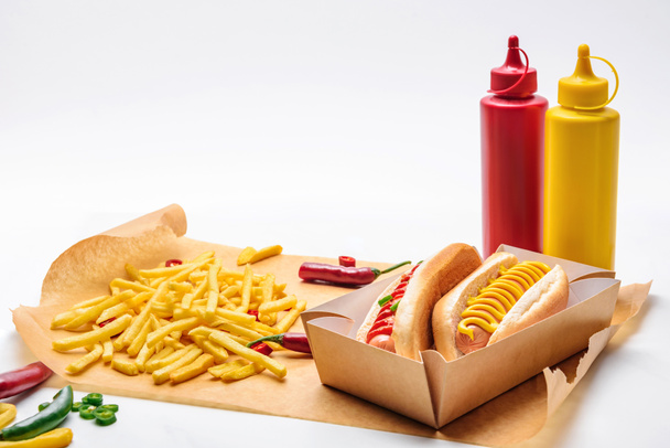 close-up shot of tasty hot dogs with mustard and ketchup on paper with fries on white - Fotografie, Obrázek