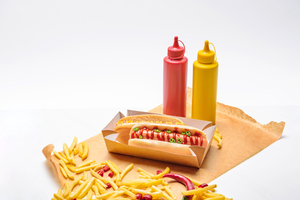 close-up shot of hot dogs with french fries, mustard and ketchup on paper on white surface - Foto, afbeelding
