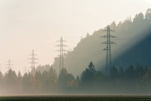 lignes électriques et treillis traverse un matin brumeux dans une vallée de montagne avec forêt de couleur automne tout autour
 - Photo, image