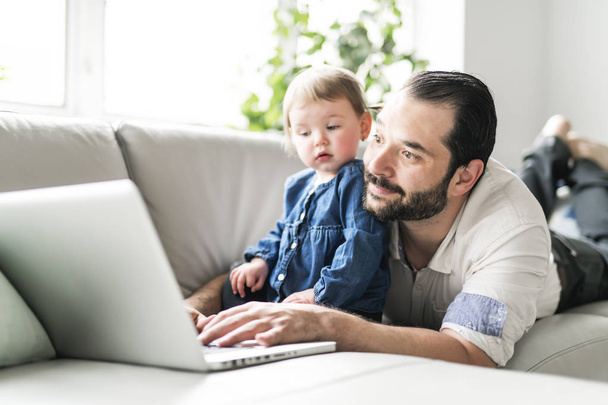 Busy father working on laptop with baby in front - Foto, immagini