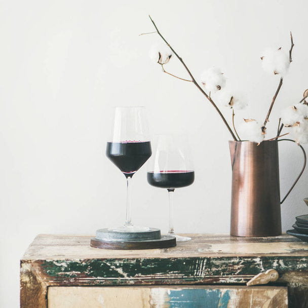 Two glasses of red wine and flowers over rustic kitchen countertop, white background behind, copy space, square crop. Wine shop, winery, bojole nouveau holiday concept - Foto, afbeelding