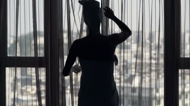 Žena v ručníku představí záclony a obdivovat výhled z okna doma - Záběry, video
