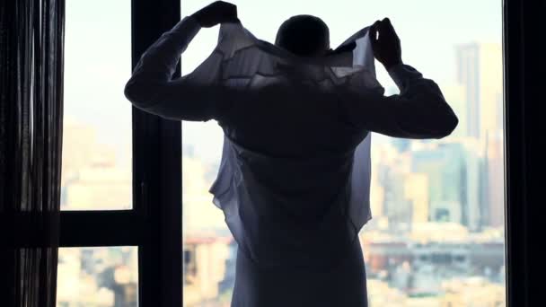 Businessman in towel putting on shirt by window at home, super slow motion 240fps - Materiał filmowy, wideo