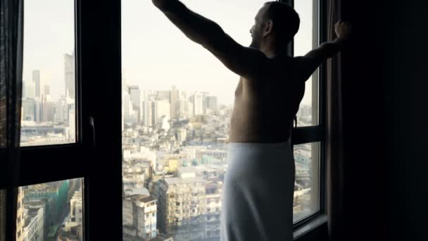 Man in towel stretching arms, neck and admire view from window at home - Video