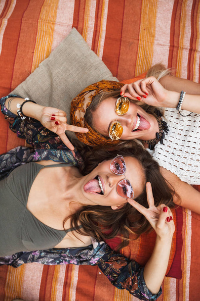Photo from top of two cute hippie girls smiling and lying on blanket outdoor head to head - Foto, Bild