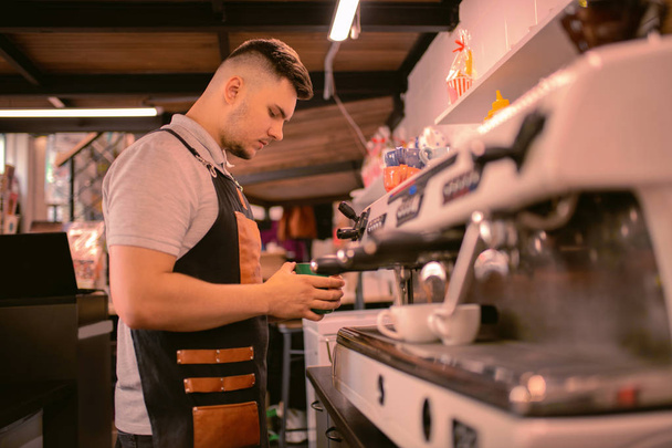 Concentrated young barista standing near coffee machine - Fotoğraf, Görsel