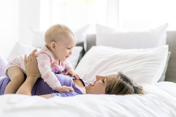 Happy mother with baby lying on bed at home - Foto, immagini