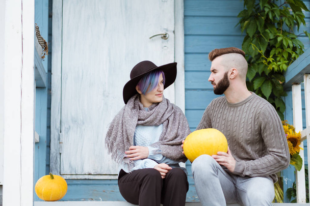 Young woman and man, family, sitting on porch of village house with pumpkins. - Photo, image