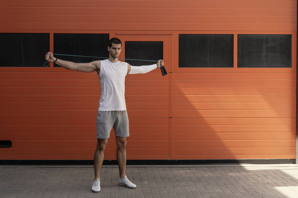 Portrait of muscular young man exercising with jumping rope on orange wall background - Photo, Image