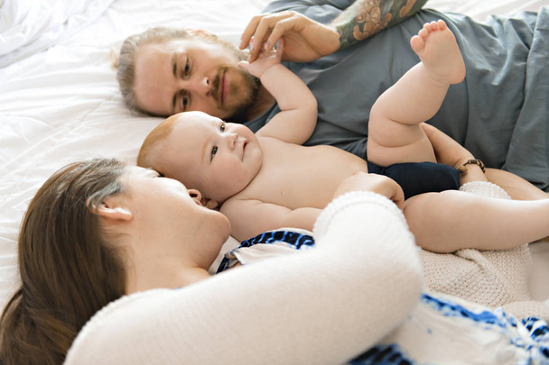 Portrait of happy young parents with baby in the bed at home - Photo, Image