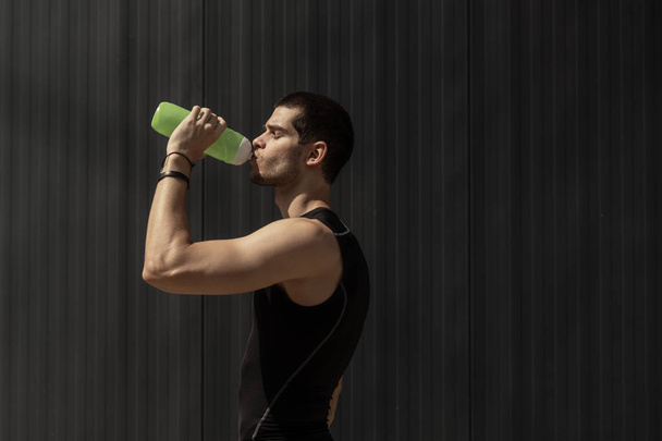 Спортивная модель мужчина пьет воду из пластиковой бутылки на сером фоне с копировальным пространством. Портрет мускулистый человек берет перерыв, чтобы увлажнить свое тело после тренировки
. - Фото, изображение