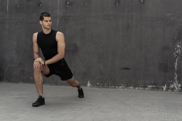 Handsome, athletic man warming up stretching before the training, with gray walls in the background. Healthy lifestyle and sportswear advertising. - Foto, Imagem