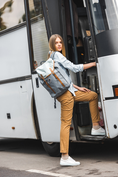 attractive young woman with backpack walking into travel bus at urban street - Foto, immagini