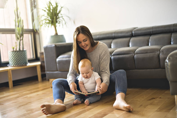 Mulher bonita com seu bebê e um livro na sala de estar
 - Foto, Imagem