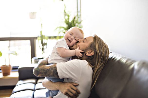 A father playing with baby daughter on sofa at home - Foto, Imagen