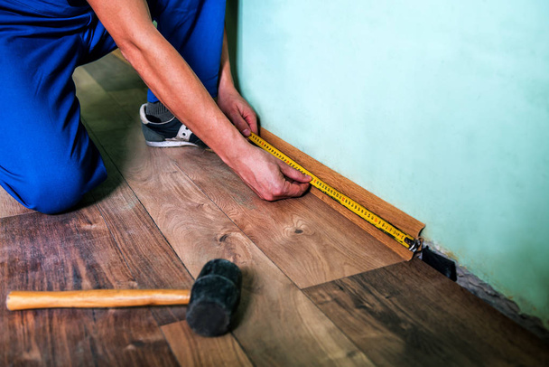 professional master in blue overalls make new laminated floor and skirting board - Foto, afbeelding