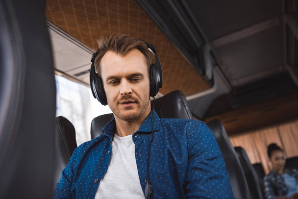 adult man in headphones listening music and looking down during trip on travel bus  - Photo, image