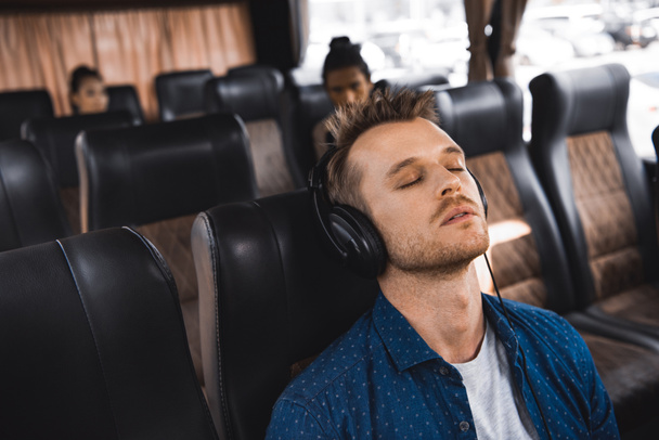 adult man in headphones listening music and sleeping during trip on bus  - Фото, изображение