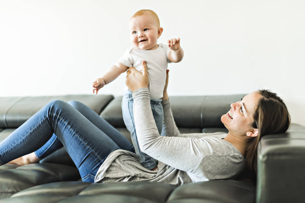 mother with baby daughter on sofa at home - Foto, imagen