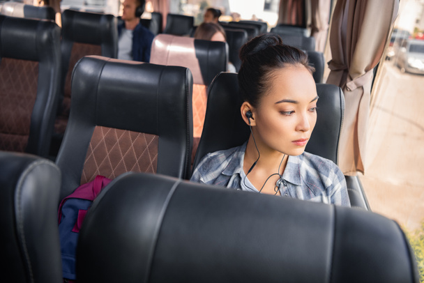 όμορφη γυναίκα της Ασίας ακούγοντας μουσική στα ακουστικά κατά τη διάρκεια ταξιδιού σε λεωφορείο ταξιδιωτικό  - Φωτογραφία, εικόνα