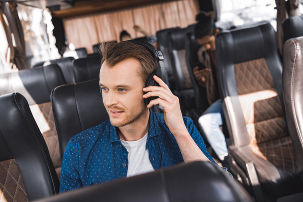 handsome male tourist in headphones listening music and looking away during trip on travel bus  - Фото, изображение