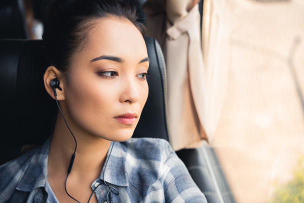 close up portrait of asian woman listening music in earphones and looking away during trip on travel bus  - 写真・画像