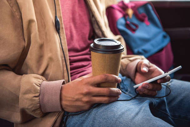 обрезанный образ человека с одноразовой чашки кофе с помощью смартфона во время поездки на автобусе
 - Фото, изображение