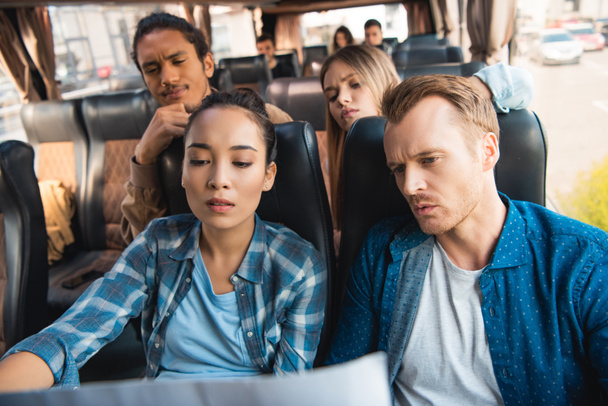 pensive multiethnic tourists looking at map during trip on travel bus - Photo, Image
