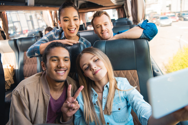 young mixed race man doing peace sign with friends taking selfie on smartphone during trip on travel bus - Фото, зображення