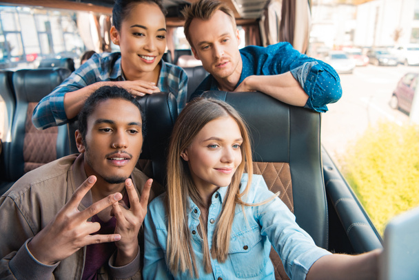 happy multiethnic friends taking selfie on smartphone during trip on travel bus - Photo, Image