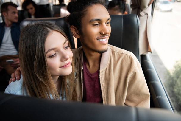 multiethnic smiling couple looking at window during trip on travel bus - Foto, Bild