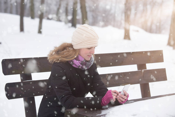 Dívka pomocí smartphone v parku v zimní sezóně. - Fotografie, Obrázek