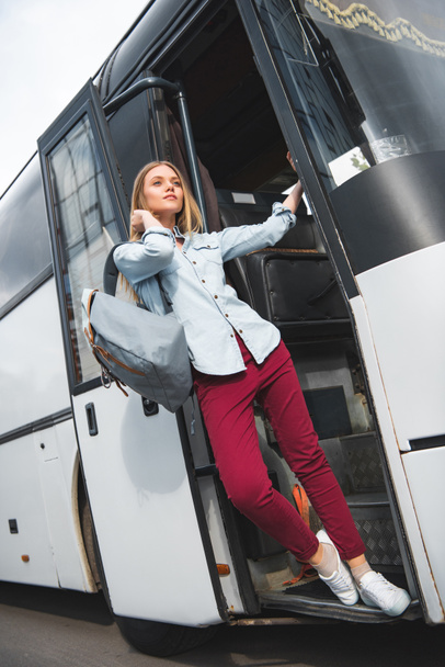 confident female tourist with backpack posing near travel bus at city street - Foto, Imagen