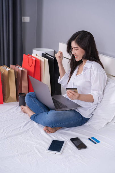 fröhliche Frau nutzt Laptop zum Online-Shopping auf dem Bett - Foto, Bild