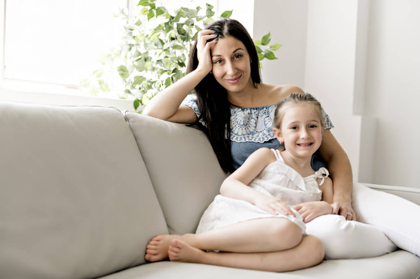 Portrait of beautiful mother and her little daughter sitting together on couch - Zdjęcie, obraz