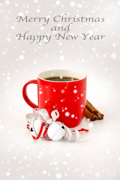 Red mug filled with black coffee and decorated with white jingle bells, silver metallic ribbon, cinnamon sticks and snowfall. Merry Christmas and Happy New Year written on the top. - Foto, imagen